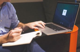 Up close image of a student writing in a notebook and using their laptop