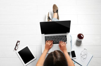 Aerial view of a student that is sitting on the floor and doing school work on a laptop