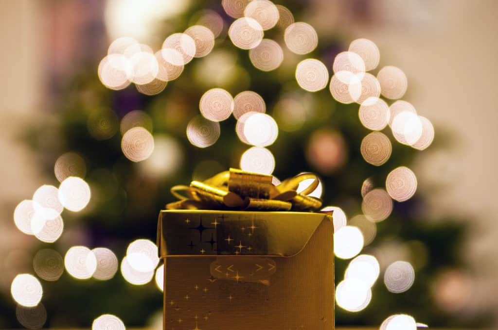 A gold christmas gift with a christmas tree in the background