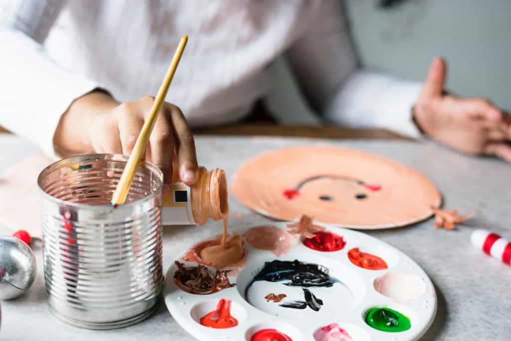 a Closeup of someone painting a smiley face with paints and a paintbrush cup