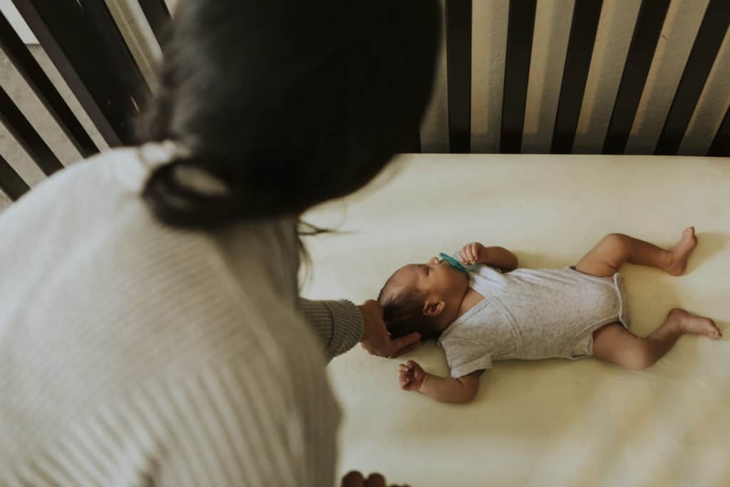 Mother is looking at her baby in a crib